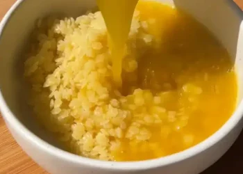 A bowl of cooked rice is topped with a stream of raw beaten egg yolk on a wooden surface, reminiscent of traditional Japanese tamago kake gohan—a comforting dish akin to the warmth found in Italian Penicillin Soup.