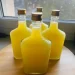 Four square glass bottles filled with bright yellow liquid, crafted from a traditional limoncello recipe and sealed with gold screw caps, are arranged on a wooden surface near a window.