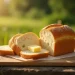 A loaf of bread is partially sliced on a wooden cutting board outdoors, with a couple of slices topped with pats of butter—a perfect outdoor boys bread recipe moment set against a sunny, blurred backdrop of green grass.