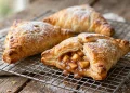 Golden flaky apple turnovers with puff pastry dusted with powdered sugar on a cooling rack