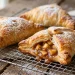 Golden flaky apple turnovers with puff pastry dusted with powdered sugar on a cooling rack