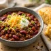Bowl of beef chili con carne topped with sour cream, cheddar and green onions