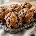 Tall blueberry muffins with golden cinnamon streusel topping and bursting berries in a muffin tin