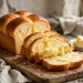 A golden buttery brioche loaf sliced to show its feathery tender yellow crumb, on a wooden cutting board