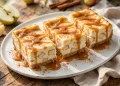 Caramel apple cheesecake bars drizzled with caramel sauce on a white platter