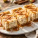 Caramel apple cheesecake bars drizzled with caramel sauce on a white platter