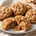Caramel-stuffed apple cookies on a plate, one broken open showing gooey caramel