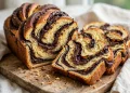 Sliced chocolate babka with dramatic dark fudgy ribbons marbled through golden crumb on a wooden board