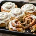Pan of golden cinnamon rolls with cream cheese frosting, one roll pulled apart showing the gooey swirl
