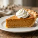 A slice of classic pumpkin pie topped with whipped cream on a white ceramic plate