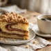 A slice of sour-cream cinnamon streusel coffee cake showing the thick cinnamon swirl and crumbly streusel topping, beside a cup of coffee
