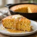 Golden slice of skillet cornbread with melting honey butter, cast iron skillet in background