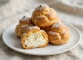 Cream puffs filled with whipped cream, dusted with powdered sugar, stacked on a white plate