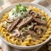Creamy beef stroganoff with mushrooms over egg noodles in a white bowl