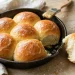 Pan of soft golden dinner rolls brushed with melted butter, one roll pulled out showing fluffy interior