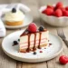 A slice of layered cheesecake topped with raspberry, blackberry, and chocolate sauce sits on a plate with scattered berries. Perfect for fans of easy desserts, this treat shines alongside a fork, strawberries, and another dessert in the background.