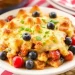 A plate of baked casserole topped with melted cheese, garnished with fresh blueberries, cherry tomatoes, and green herbs—perfect for fourth of July casserole recipes—served on a white dish with a red and white striped cloth in the background.