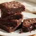 Stack of fudgy dark chocolate brownies with flaky sea salt on a white plate