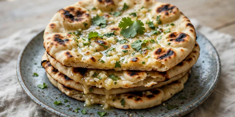 A stack of homemade garlic naan with charred spots, brushed with garlic butter and sprinkled with fresh cilantro