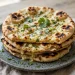 A stack of homemade garlic naan with charred spots, brushed with garlic butter and sprinkled with fresh cilantro
