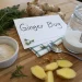 Fresh ginger root, sliced ginger, a jar of sugar, powdered ginger, herbs, and a spoon arranged on a wooden surface with a card labeled Ginger Bug—perfect ingredients for trying your own ginger bug recipe.