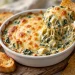 Hot spinach artichoke dip in a white baking dish with a golden cheese top, served with tortilla chips