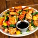 A plate of glazed hibachi chicken recipe pieces with mixed vegetables, including bell peppers, mushrooms, green beans, and yellow squash, garnished with chopped green onions and served with a small cup of soy sauce.