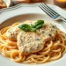 A plate of marry me chicken pasta topped with creamy chicken and fresh basil sits beside slices of bread and a glass of white wine on a softly lit table.