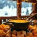 A pot of steaming cheese fondue made from an authentic Swiss fondue recipe, with pieces of bread arranged around it, set on a wooden table in a cozy cabin and snowy mountains visible through the window in the background.