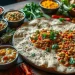 A large flatbread topped with bean curry and garnished with cilantro is surrounded by small bowls of colorful chutneys and vegetables, presenting a beautiful spread inspired by vegan Ethiopian recipes on a rustic wooden table.