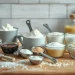 Various baking ingredients such as flour, sugar, rice, cocoa, and butter are arranged in cups and bowls on a wooden kitchen counter, perfect for practicing Cooking and Baking Conversions with measuring spoons and utensils in the background.