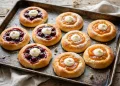 Golden kolaches on a baking tray with glossy cherry and apricot fruit fillings and cream cheese centers