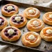 Golden kolaches on a baking tray with glossy cherry and apricot fruit fillings and cream cheese centers