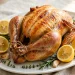 Whole golden lemon herb roast chicken with lemon halves and fresh herbs on a platter