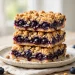 Blueberry crumble bars stacked on a plate showing jammy filling