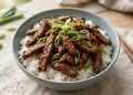 Mongolian beef stir-fry with glossy glazed flank steak strips and green onions over rice