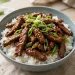 Mongolian beef stir-fry with glossy glazed flank steak strips and green onions over rice