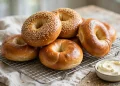 Glossy golden bagels, some topped with sesame seeds, piled on a wire cooling rack