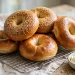 Glossy golden bagels, some topped with sesame seeds, piled on a wire cooling rack