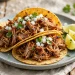 Crispy pork carnitas tacos in warm corn tortillas topped with diced onion and cilantro