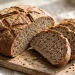 A rustic round rye bread loaf with a deeply scored crust, sliced to show an earthy crumb dotted with caraway seeds