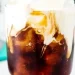 A close-up of a glass filled with iced coffee, topped with a layer of cream swirling into the dark liquid, creating a marbled effect reminiscent of a Dirty Soda fusion.