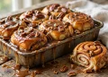 Golden caramel pecan sticky buns fresh from the oven, glistening with buttery caramel sauce, one bun pulled apart showing the soft cinnamon swirl