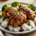 Glazed teriyaki chicken thighs over white rice with broccoli and sesame seeds