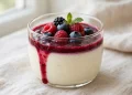 Creamy vanilla bean panna cotta topped with berry coulis in a glass