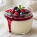 Creamy vanilla bean panna cotta topped with berry coulis in a glass